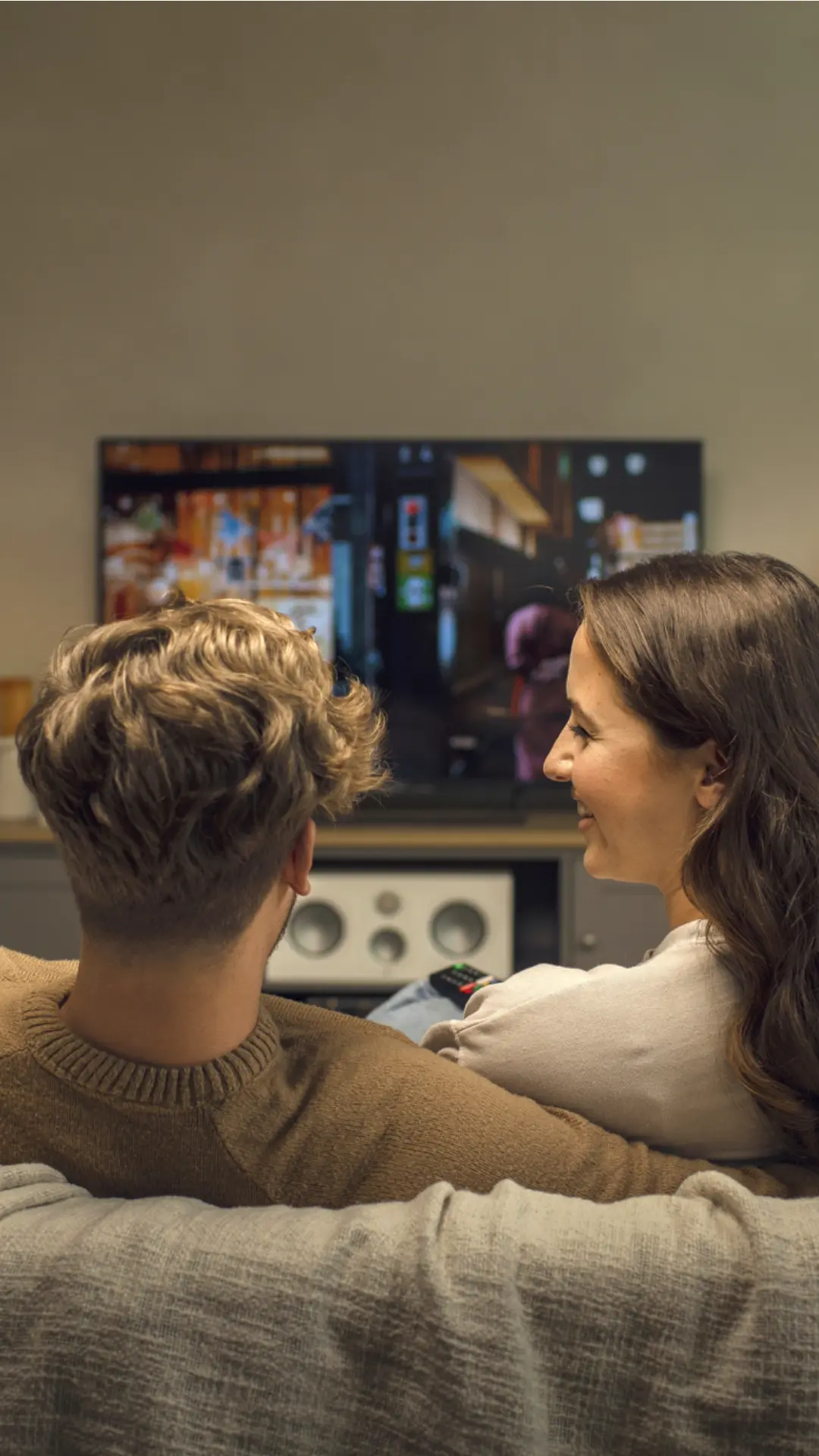 Ein junges Paar auf der Couch. Im Hintergrund lässt sich der weiße Monitor Audio Silver C250 7G Center Lautsprecher erkennen.