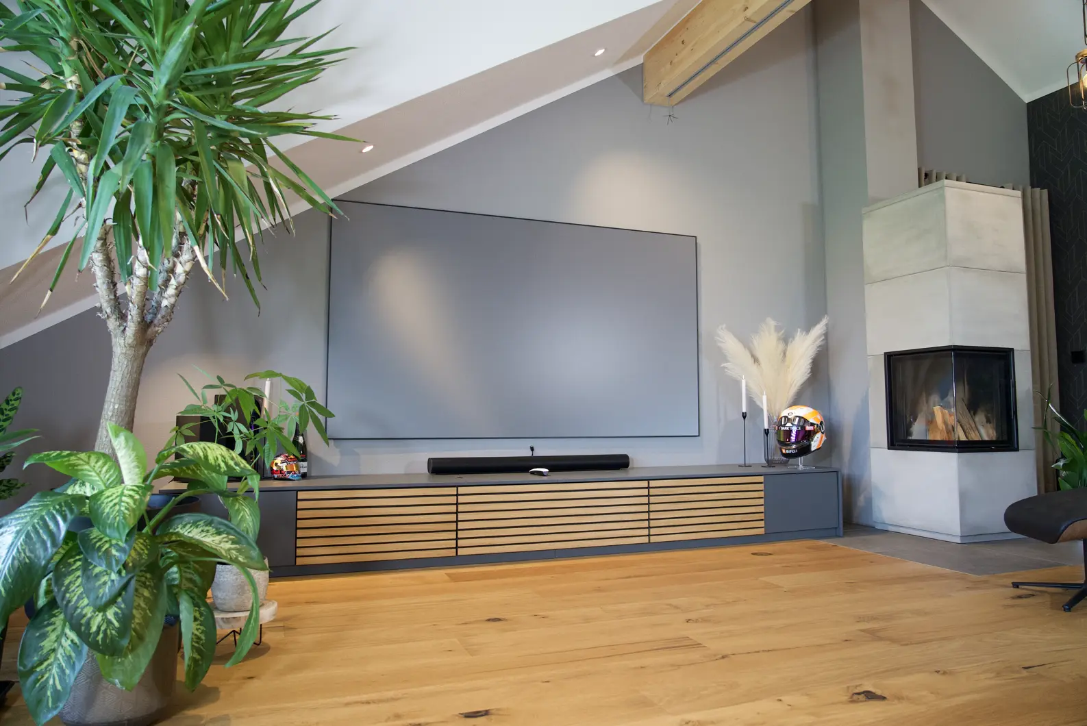 Heimkino im Wohnzimmer made by AVITECT Studio Ingolstadt. Ein modernes Wohnzimmer mit warmen Holztönen und vielen Pflanzen. Der Laser TV ist in ein maßgeschneidertes Lowboard eingelassen und eine 100 Zoll Leinwand fügt sich elegant in das Wohnzimmer ein.