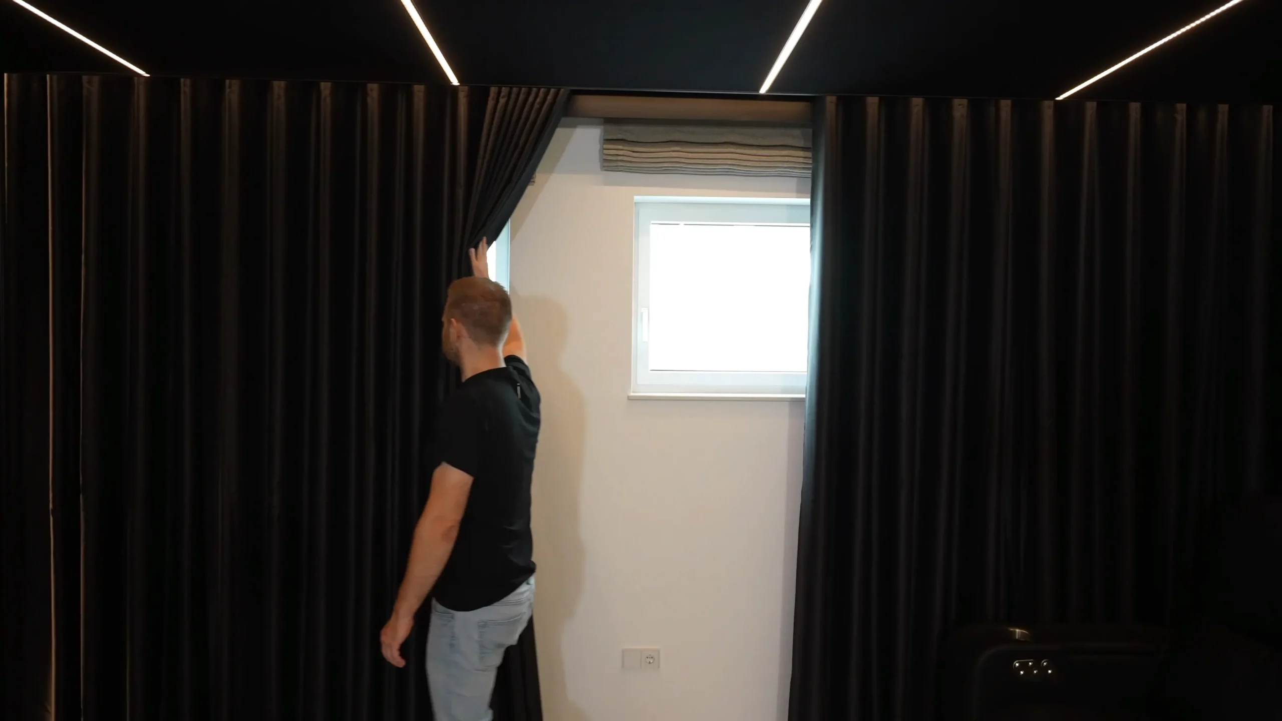 Sebastian vom AVITECT Studio Rhein-Main zeigt, dass sich hinter den Vorhängen auf der rechten Seite Fenster für die Frischluftzufuhr verbergen.