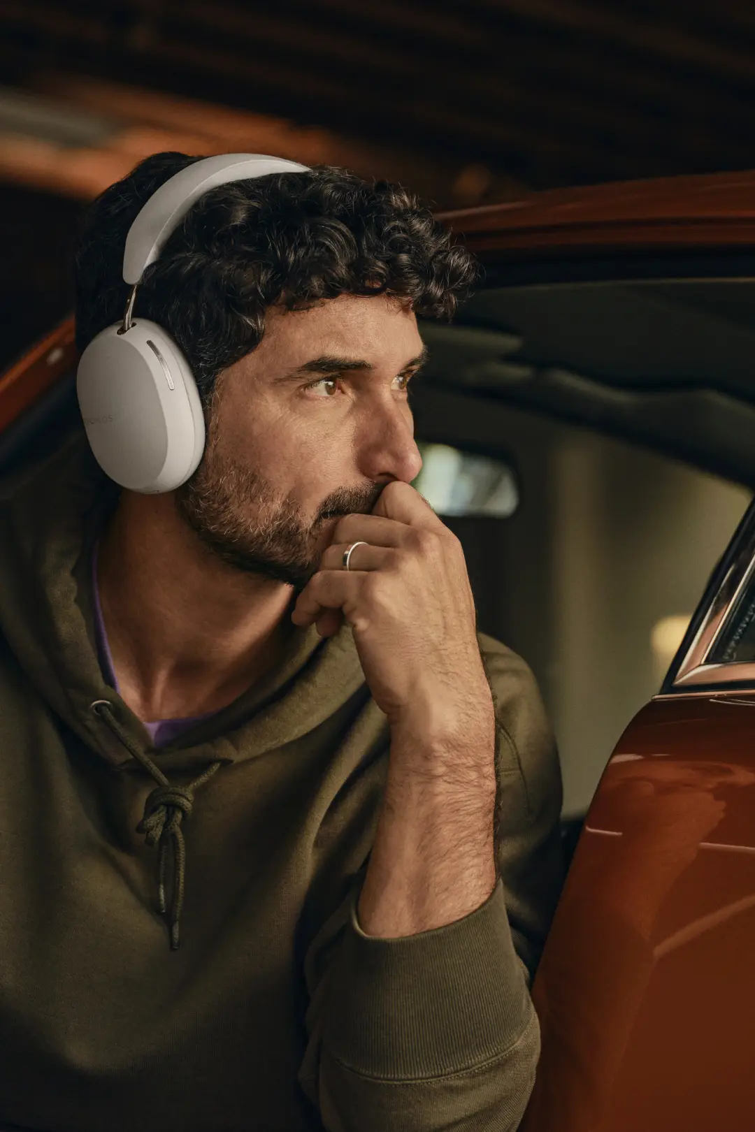 Ein Mann trägt den weißen Sonos Ace währen er in der Tür von einem Porsche Oldtimer in einer Garage sitzt und bedächtig der Musik lauscht.