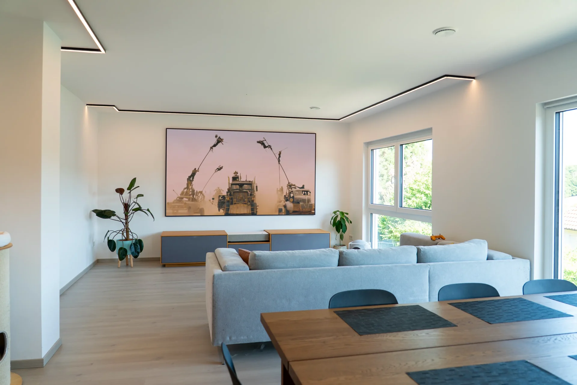 Offener Wohn-/Essbereich: AVITECT White-Cinema Lowboard vor 120″ ALR-Leinwand, graues Sofa und Holzesstisch im Vordergrund