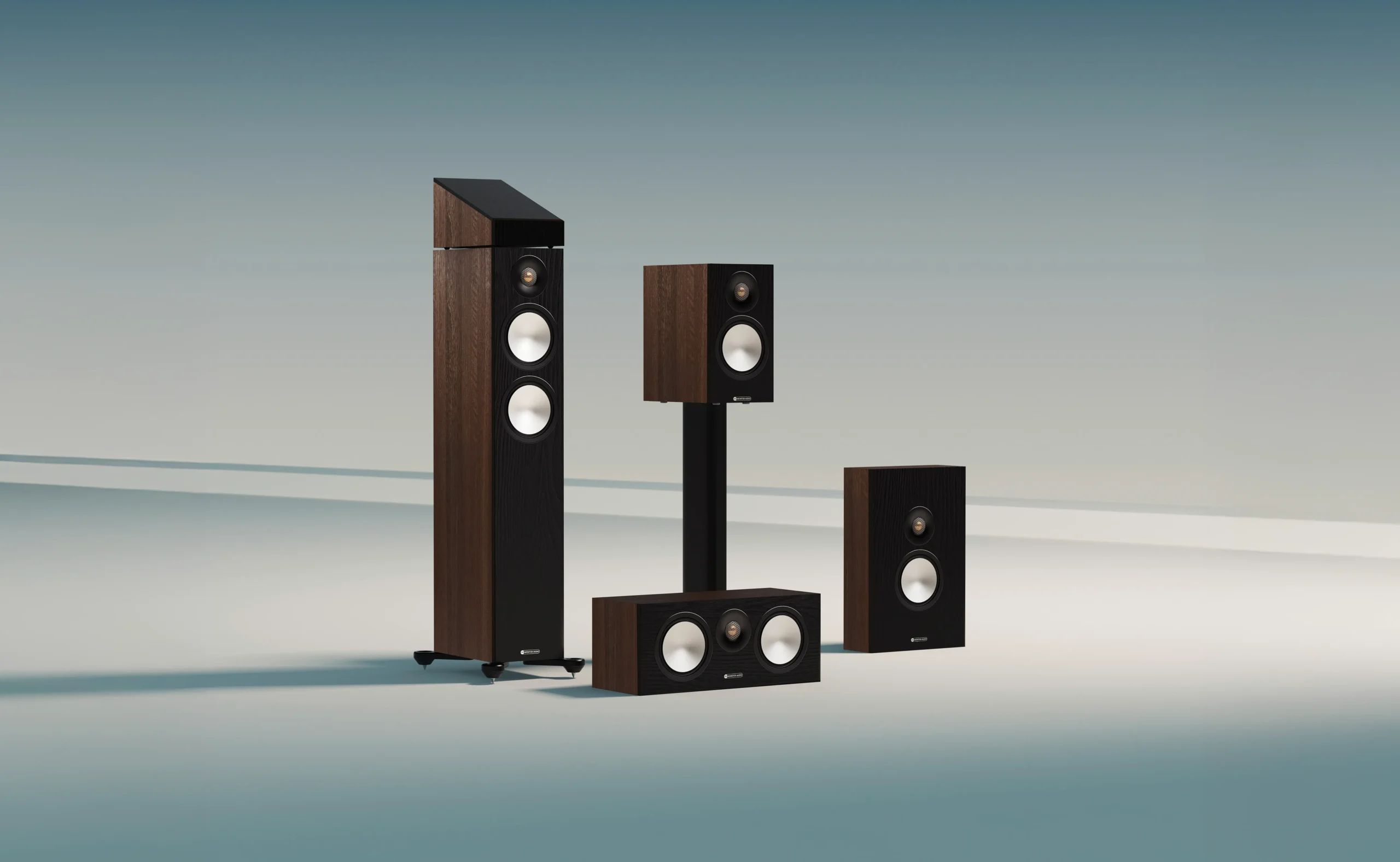 Monitor audio Bronze 7g set IN walnuss von vorne ohne Abdeckung auf blauweißem Hintergrund von links nach rechts Bronze 300 7G mit Bronze AMS 7g dann centre 7G dahinter Standlautsprecher mit bronze 50 7gdann bronze on wall 7g