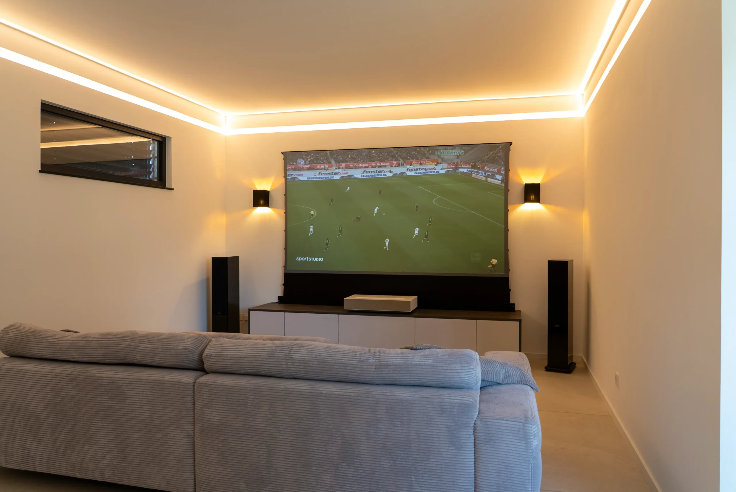 Wohnraum mit ausgefahrener Leinwand und laufender Sportübertragung, AVITECT Studio Rhein-Main