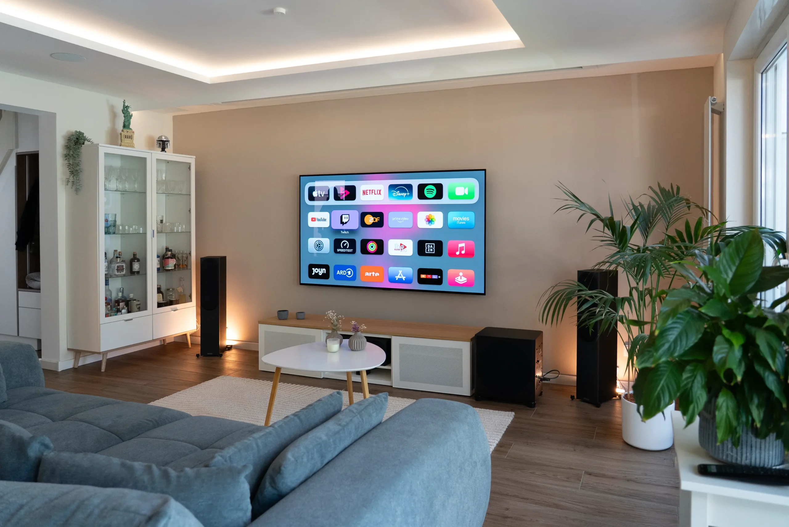 White Cinema Heimkino im Wohnzimmer mit großem OLED-TV, App-Menü aktiv, Teil der Duallösung mit Beamer und Leinwand, umgesetzt vom AVITECT Studio Aachen.