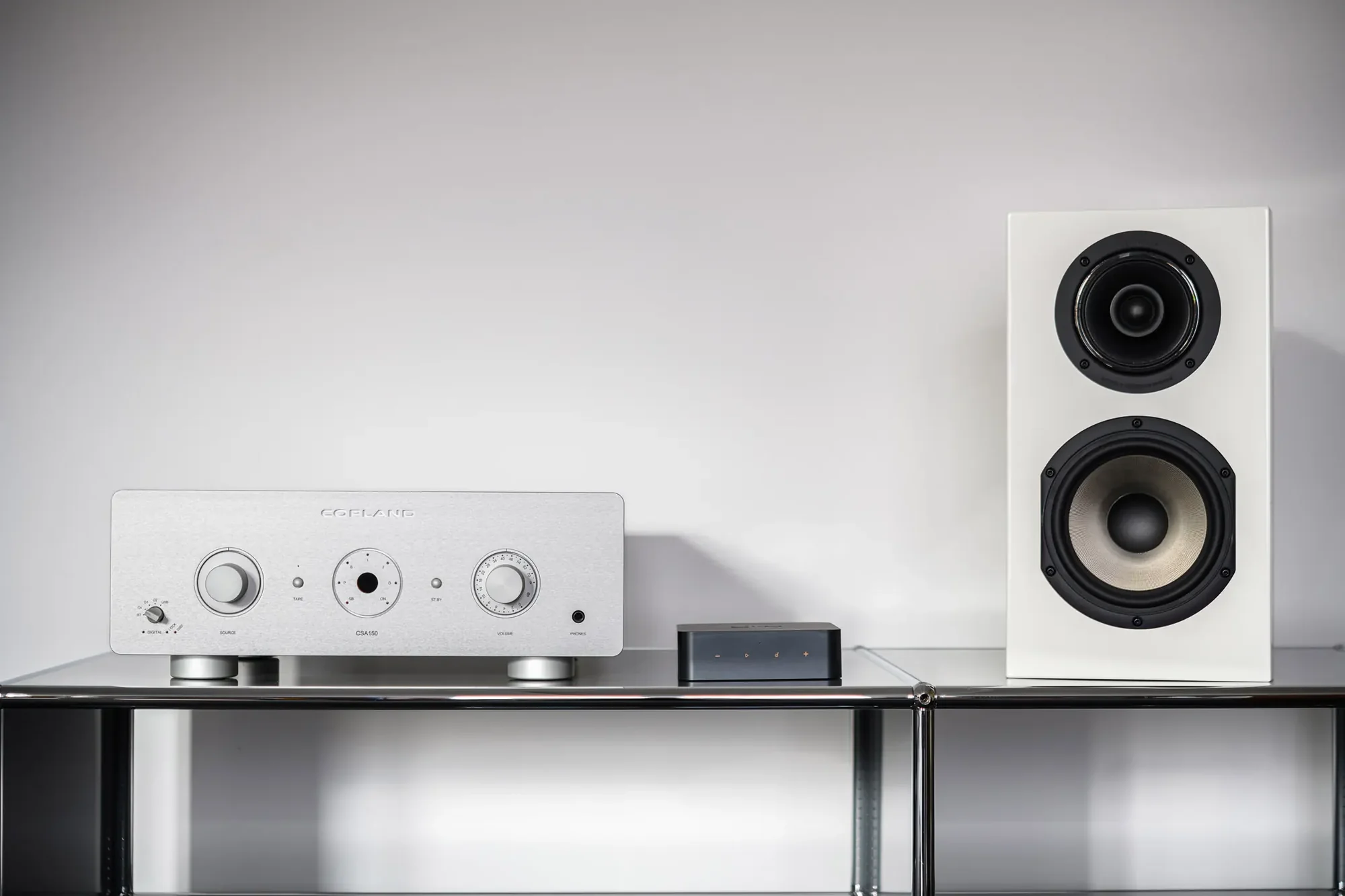 Das BIld zeigt den WiiM pro Plus streamer gemeinsam mit der Fernbedienung auf einer Oberfläche in einem HiFi-Setup mit Lautsprechern