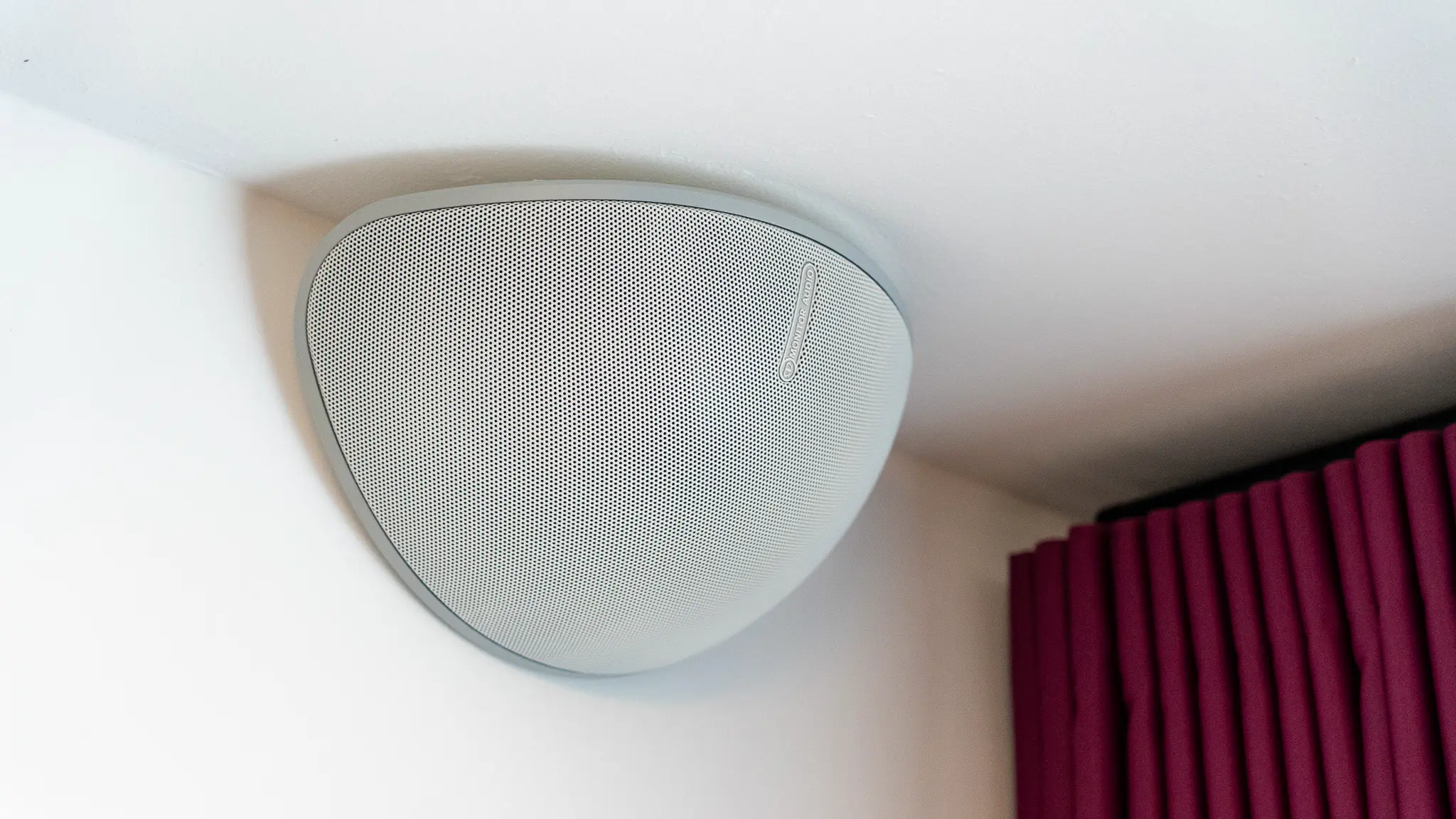 Nahaufnahme des Monitor Audio Vecta Surround-Lautsprechers über dem Vorhang – dezente, aber leistungsstarke Rear-Lösung im White Cinema.