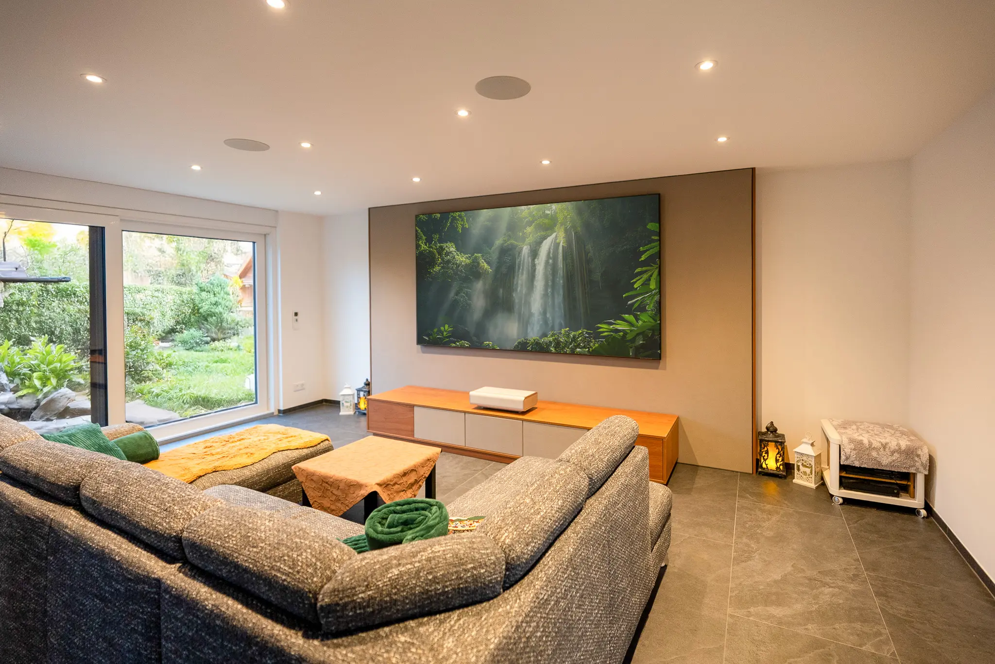 Moderne Wohnzimmergestaltung: Die Technik-Wand mit ausgeschaltetem Screen wirkt wie ein hochwertiges Design-Element gegenüber der großen Couchlandschaft.