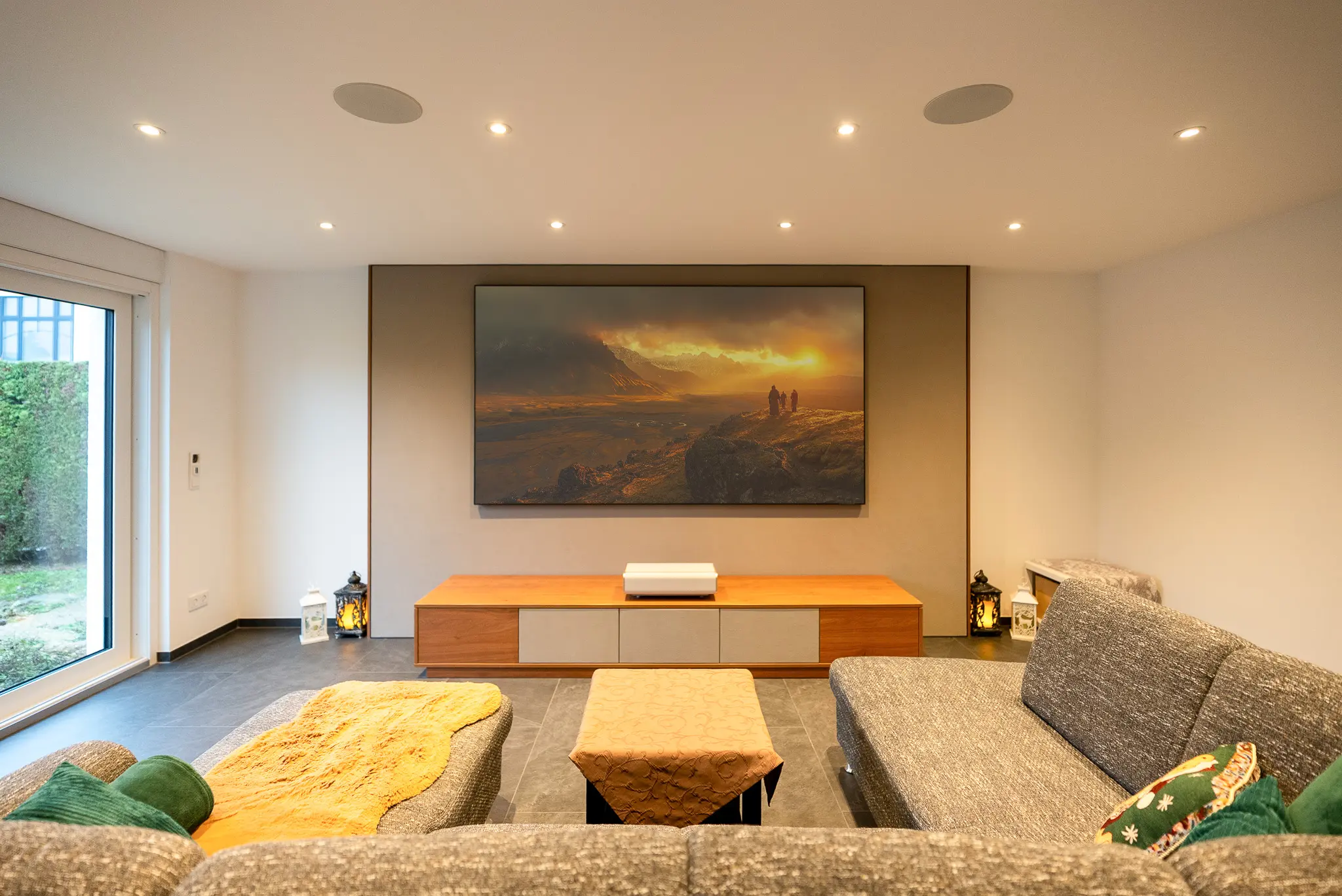 Totale Raumansicht: Das ausgeschaltete Heimkino-System fügt sich mit grauer Soundwall und warmem Holz-Lowboard elegant in das moderne Wohnambiente ein.