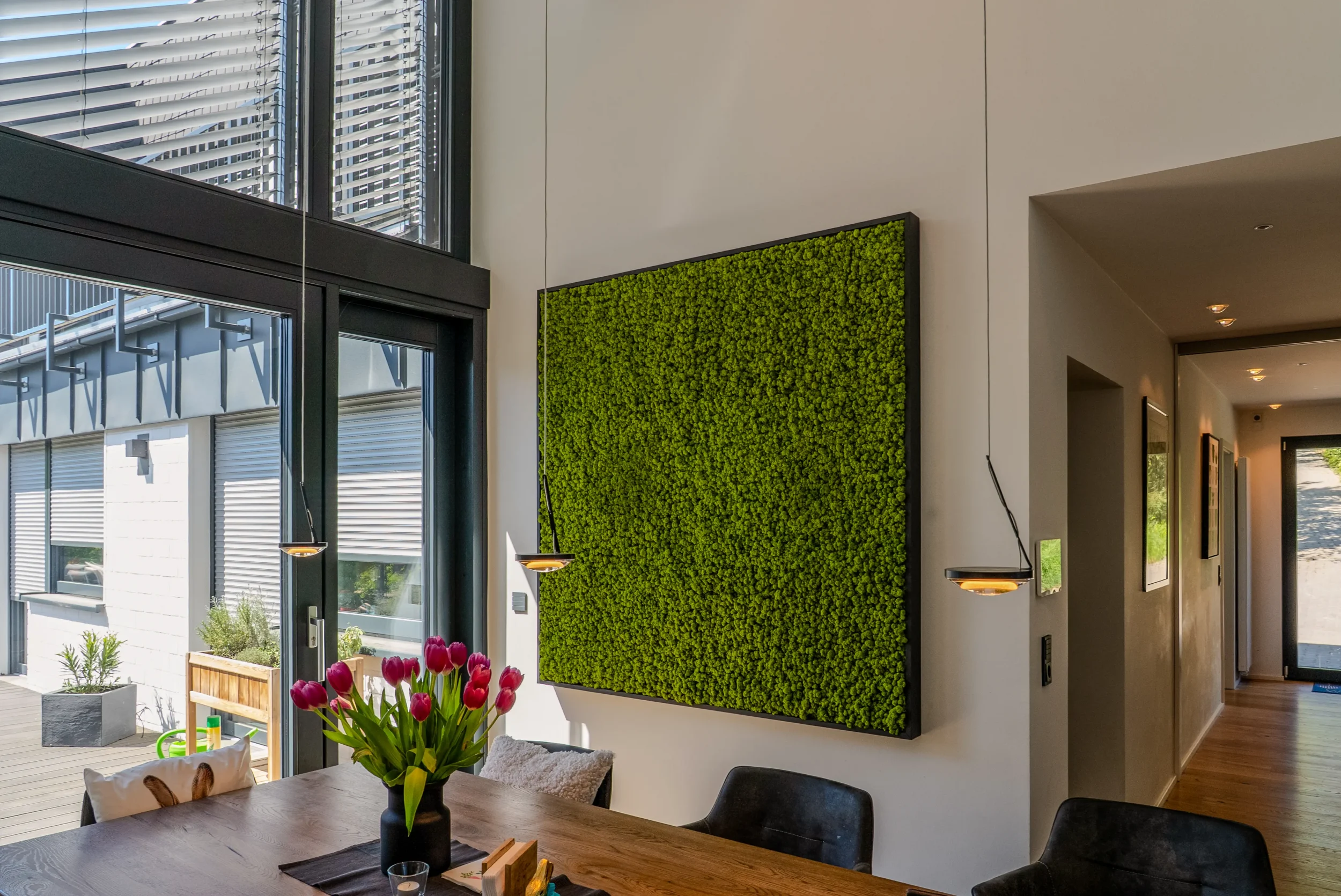 Mooswand über Holzesstisch mit rosa Tulpen und Pendelleuchten in der Raumakustik-Maßnahme Rhein-Main.