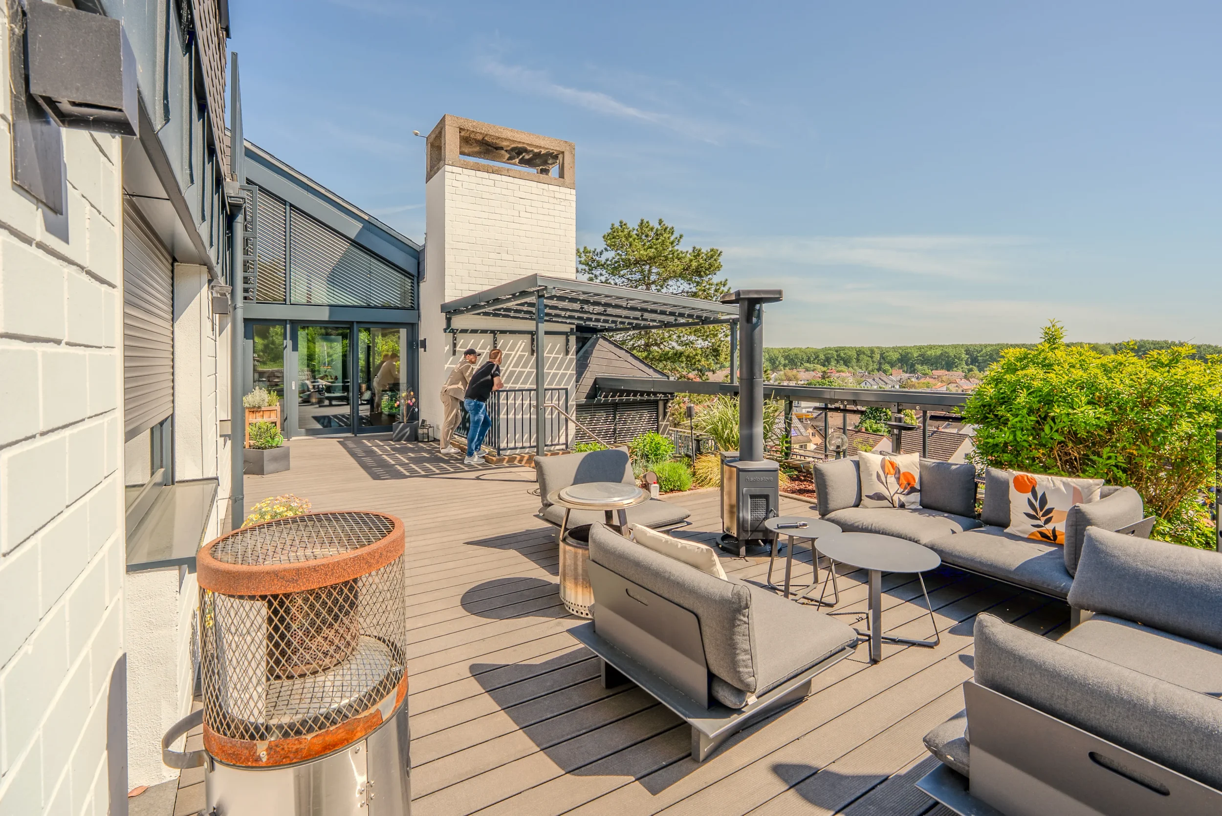 Dachterrasse mit Lounge-Möbeln, Feuerschale und Blick auf Wald und Ortschaft in der Gartenbeschallung Rhein-Main.