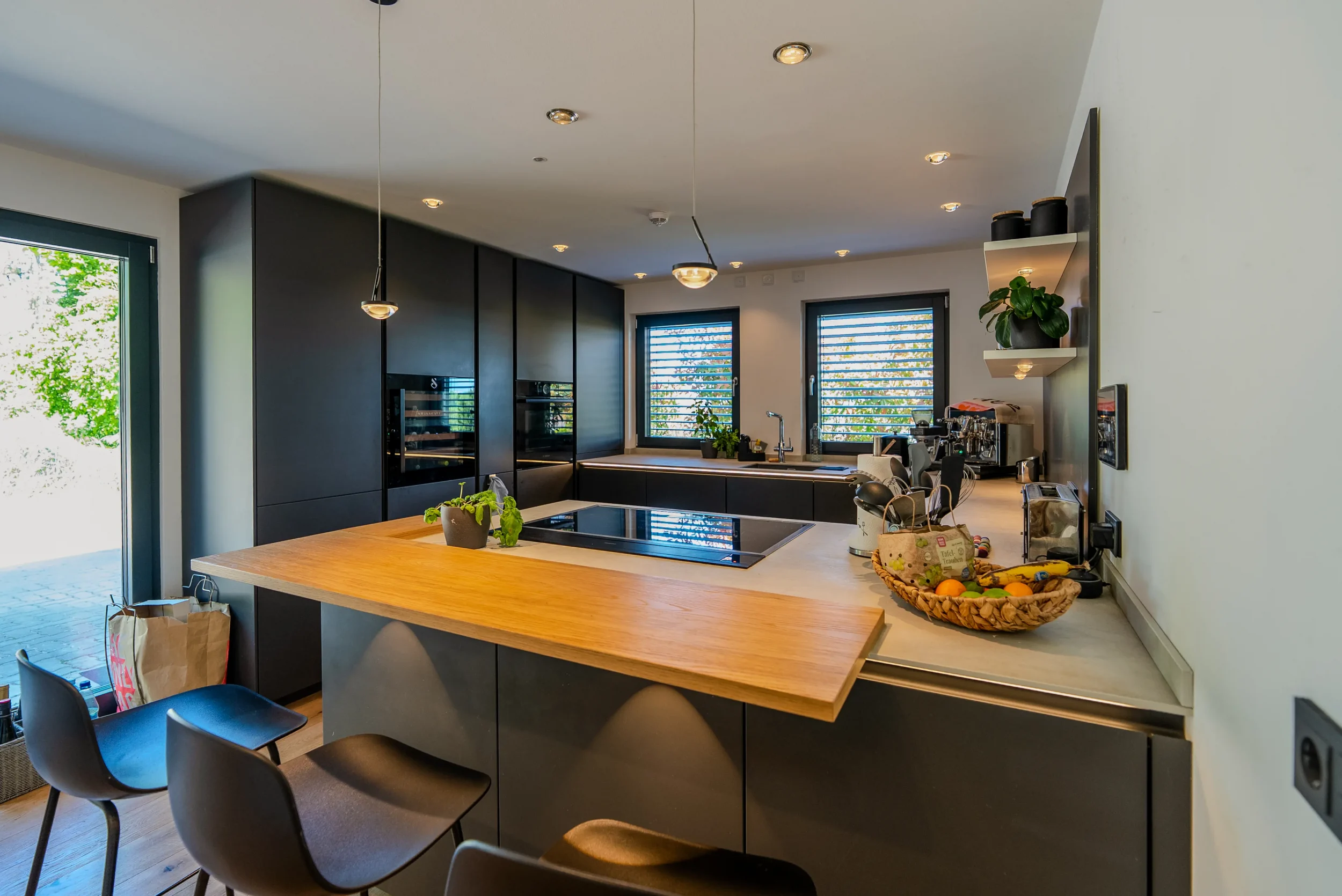 Moderne Küche mit unsichtbaren Deckenlautsprechern, dunklen Fronten und Holz-Frühstücksbar im MultiRoom-Audio-Referenzprojekt Rhein-Main.